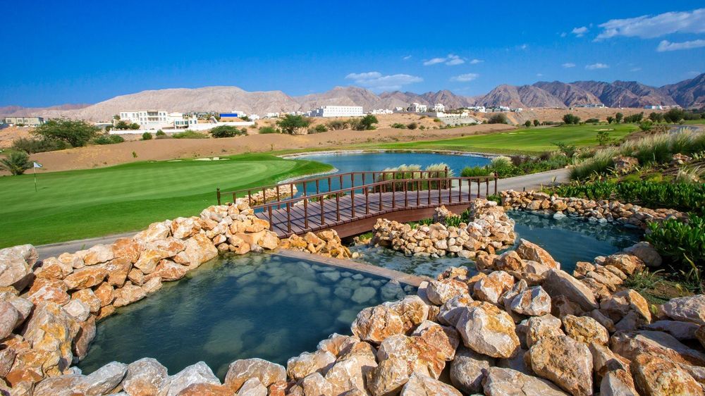 Ghala Golf Club green and water hazard framed by the Al Hajar mountains